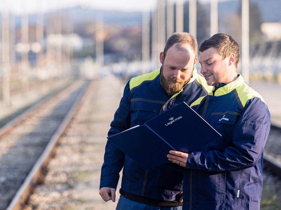 Portrait von zwei Lagermax-Mitarbeitern an den Bahnschienen im Querformat