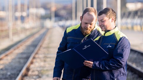 Portrait von zwei Lagermax-Mitarbeitern an den Bahnschienen im Querformat