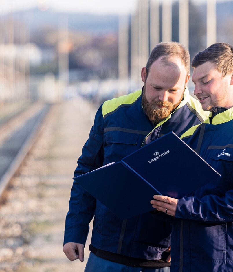 Portrait von zwei Lagermax-Mitarbeitern an den Bahnschienen im Querformat