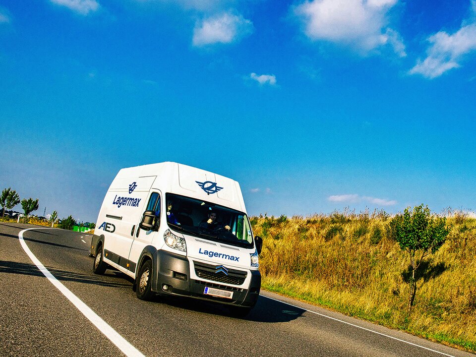 Fahrzeug für Expressdienst fährt auf Landstraße blauer Himmel im Hintergrund.