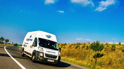 Fahrzeug für Expressdienst fährt auf Landstraße blauer Himmel im Hintergrund.
