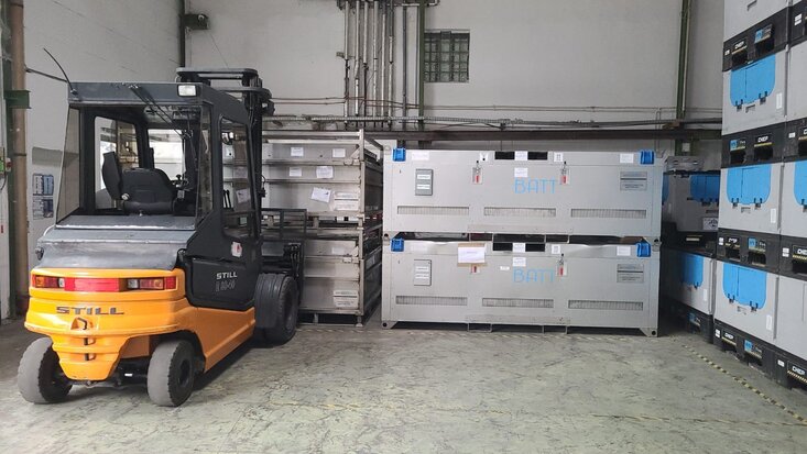 Gabelstapler in Halle vor geschlossenen Transportboxen für Batterien.