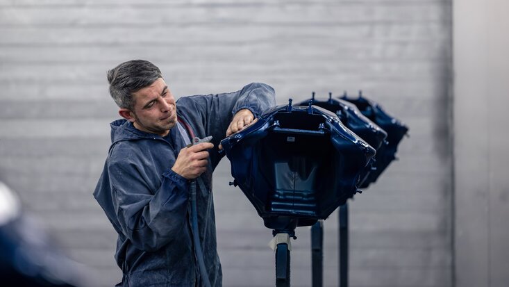 Ein Arbeiter in einer blauen Jacke bereitet einen Teil der Karosserie auf im Rahmen des Fahrzeugumbau