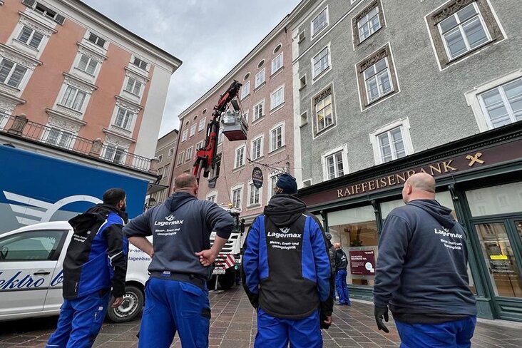 Männer beobachten Abtransport von Maschine mit Kran durch Fenster.