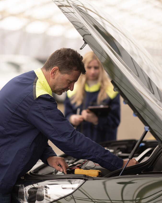 Mitarbeiter wirft einen Blick unter die Motorhaube eines Autos. 