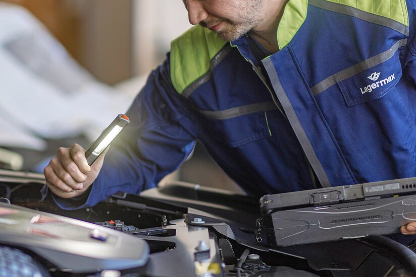 Mann mit Lampe inspiziert Motorraum.