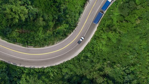 Man sieht einen blauen Lagermax LKW von oben auf einer Straße die durch einen dichten Wald führt