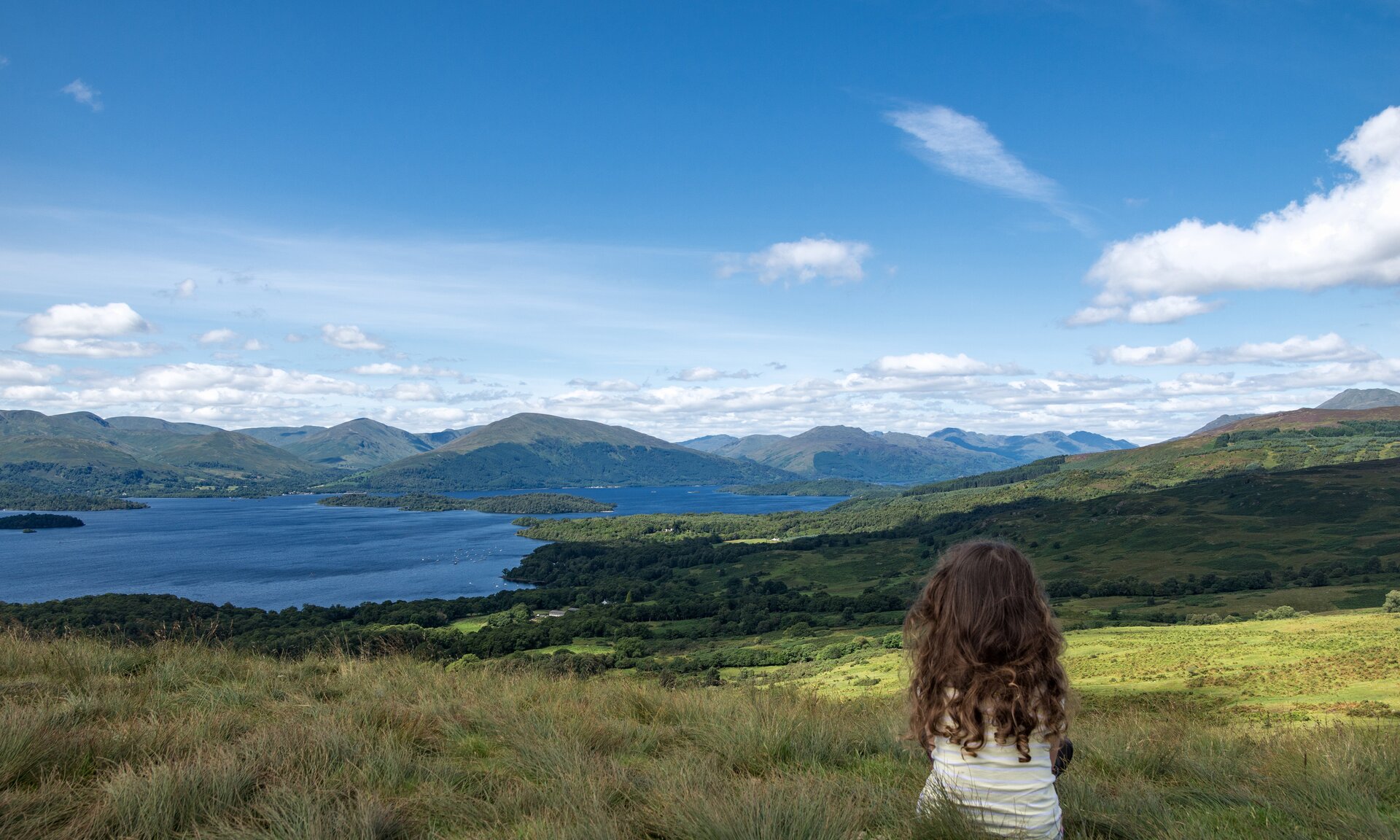 Man sieht ein junges Mädchen das auf eine herrliche Landschaft mit See blickt