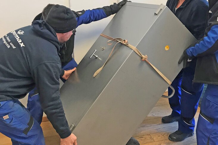 Mitarbeiter transportieren Tresor mit Sackkarre.