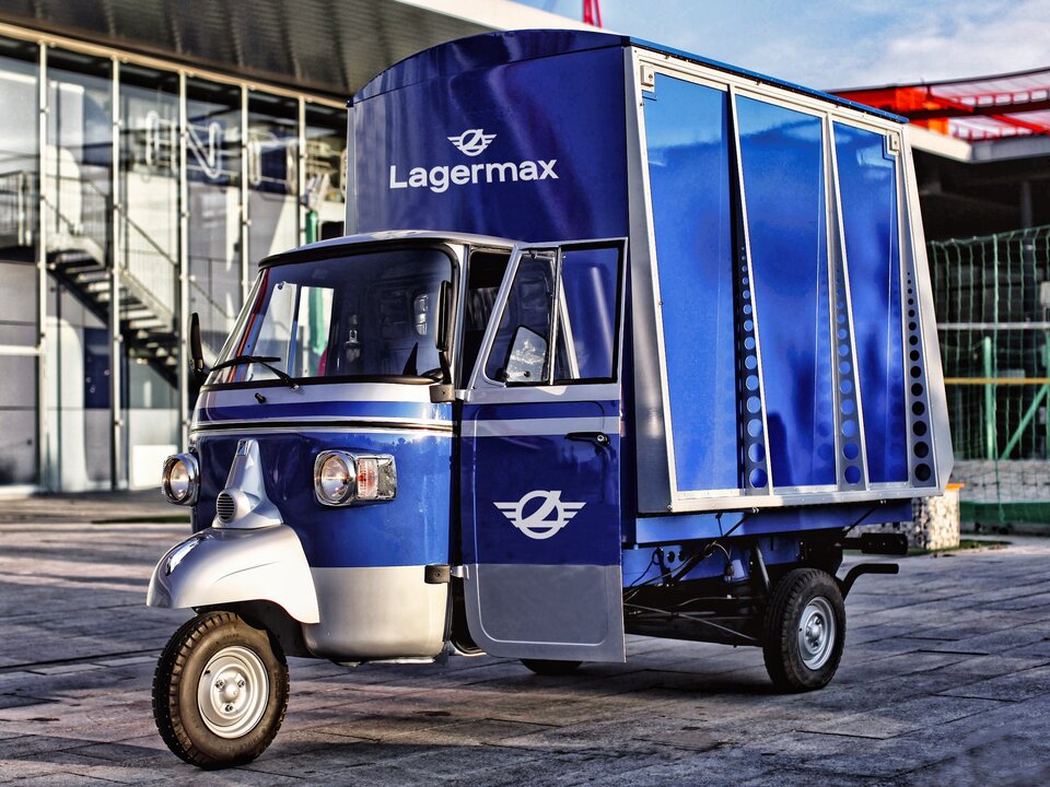 Ape Classic in blau steht vor Gebäude.