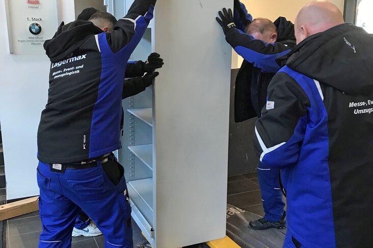 Mitarbeiter stellen Schrank auf Hubwagen - Aufnahme von hinten.
