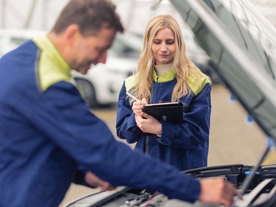 Ein Lagermax Mitarbeiter arbeitet an offener Motorhaube und eine Frau ist im Fokus.