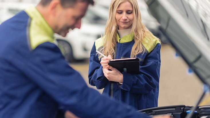 Ein Lagermax Mitarbeiter arbeitet an offener Motorhaube und eine Frau ist im Fokus.