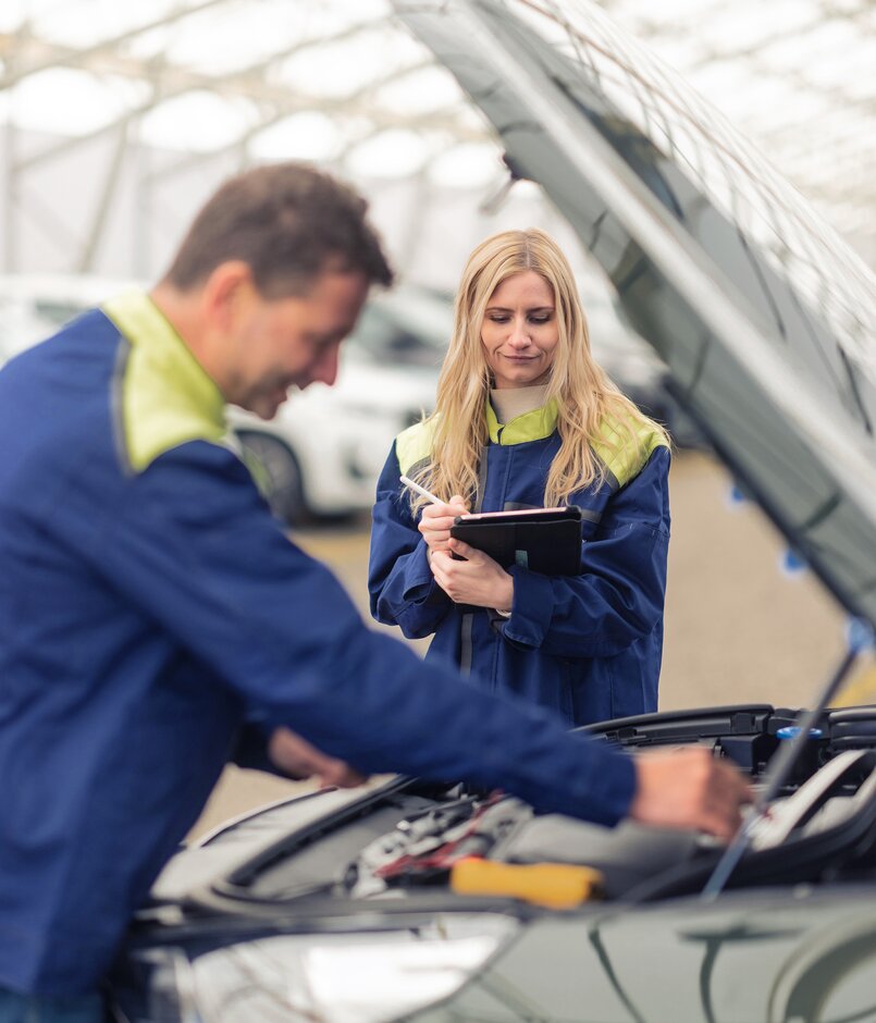 Ein Lagermax Mitarbeiter arbeitet an offener Motorhaube und eine Frau ist im Fokus.