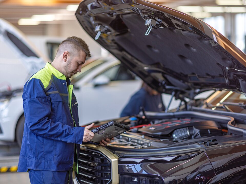 Ein Arbeiter steht mit einem Tablet neben einer offenen Motorhaube