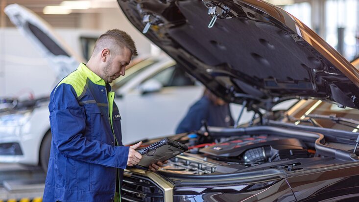 Ein Arbeiter steht mit einem Tablet neben einer offenen Motorhaube