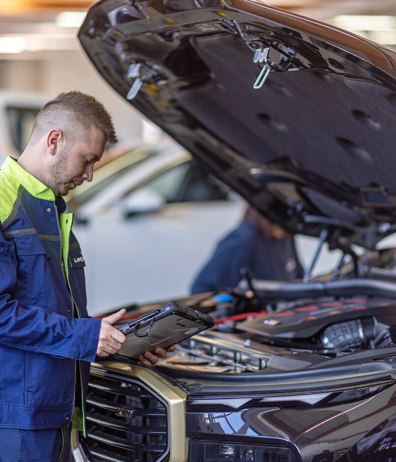 Ein Arbeiter steht mit einem Tablet neben einer offenen Motorhaube