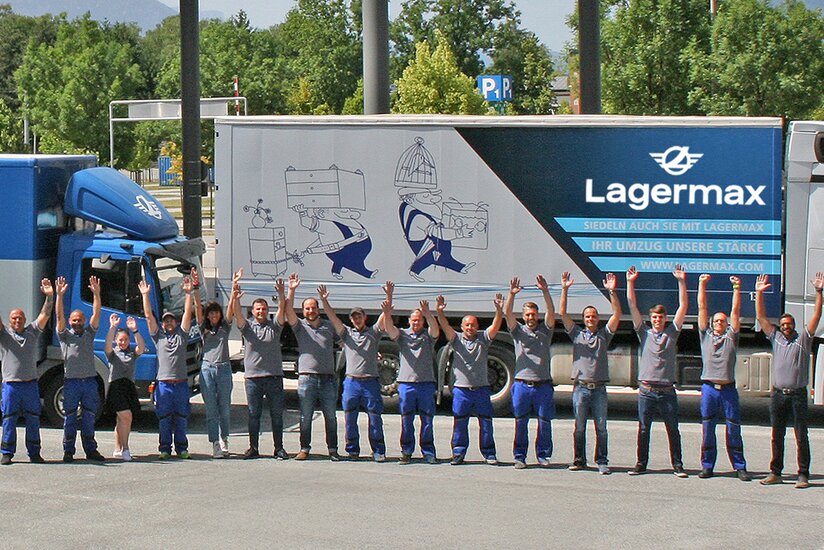 Lagermax Mitarbeiter stehen vor Lkw und jubeln.