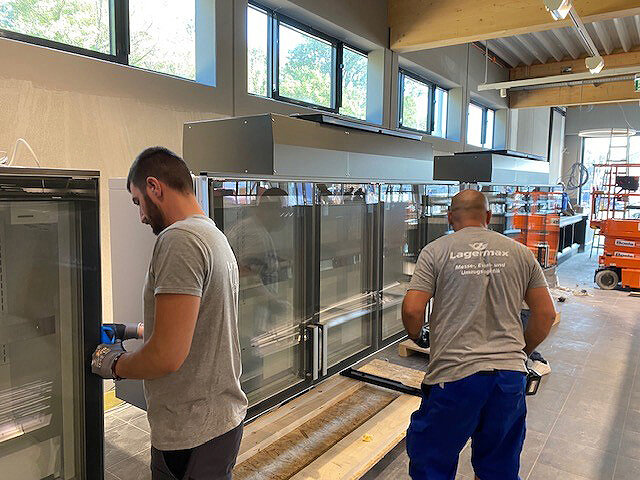 Mitarbeiter montieren Kühlgeräte in Supermarkt.