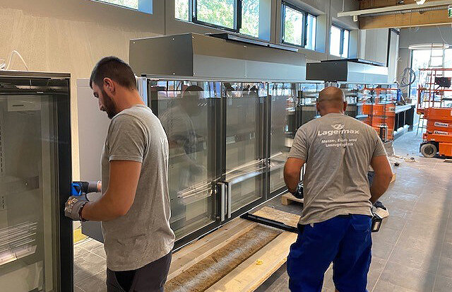 Mitarbeiter montieren Kühlgeräte in Supermarkt.