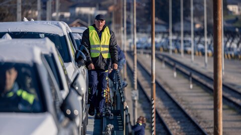 Ein Lagermax Arbeiter sitzt in Auto auf Gueterzug und Kamerafokus ist auf zweitem Arbeiter mit Schutzweste im Hintergrund.