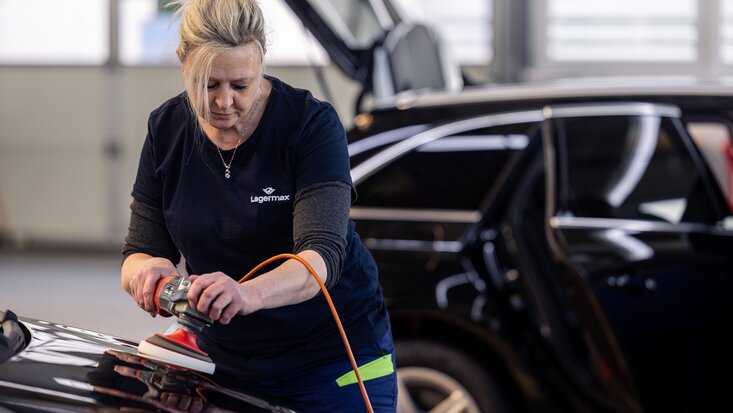 Man sieht eine Arbeiterin bei der Politur eines Fahrzeugs im Querformat