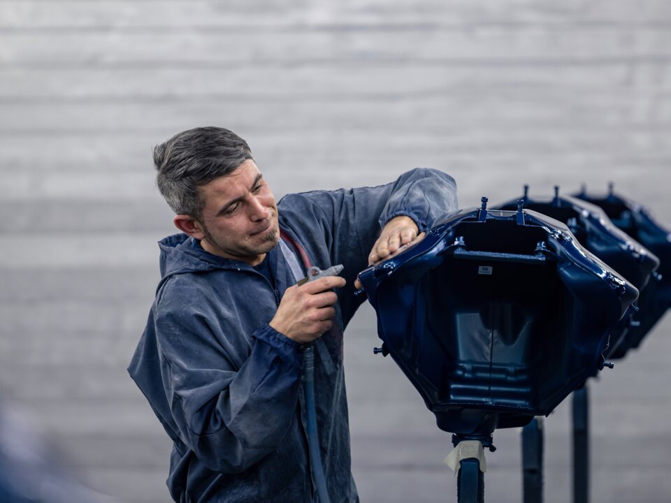 Ein Arbeiter in einer blauen Jacke bereitet einen Teil der Karosserie auf im Rahmen des Fahrzeugumbau
