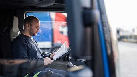 Ein Arbeiter sitzt in einer LKW Fahrerkabine und sieht sich Dokument an