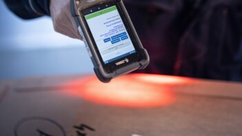 Ein Arbeiter scannt mit einem digitalen Geraet ein Paket