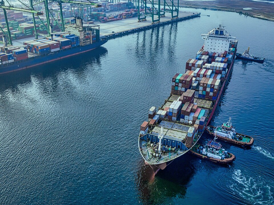 Containerschiff wird von zwei Schleppern zur Liegeposition im Hafen gebracht.