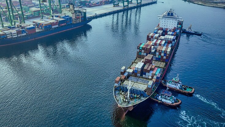 Containerschiff wird von zwei Schleppern zur Liegeposition im Hafen gebracht.