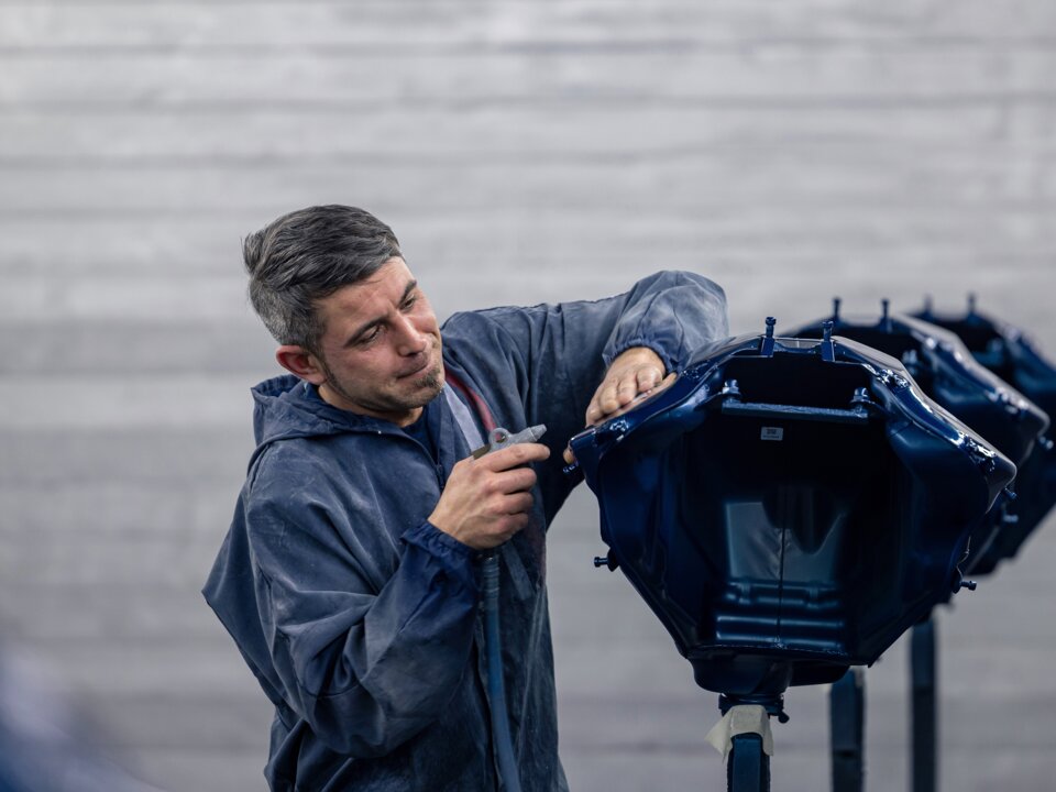 Ein Arbeiter in einer blauen Jacke bereitet einen Teil der Karosserie auf im Rahmen des Fahrzeugumbau