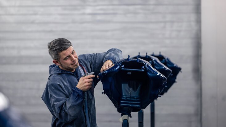 Ein Arbeiter in einer blauen Jacke bereitet einen Teil der Karosserie auf im Rahmen des Fahrzeugumbau