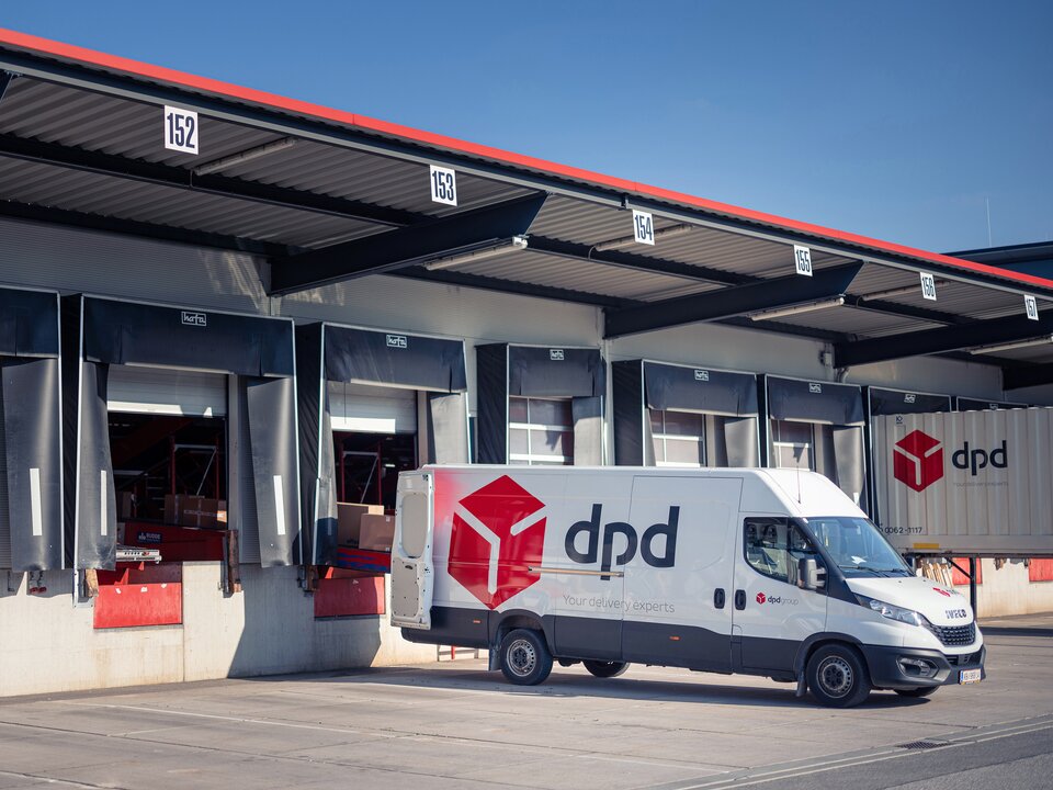 Es steht ein dpd Transporter vor einer Lagerhalle und wird mit Paketen beladen