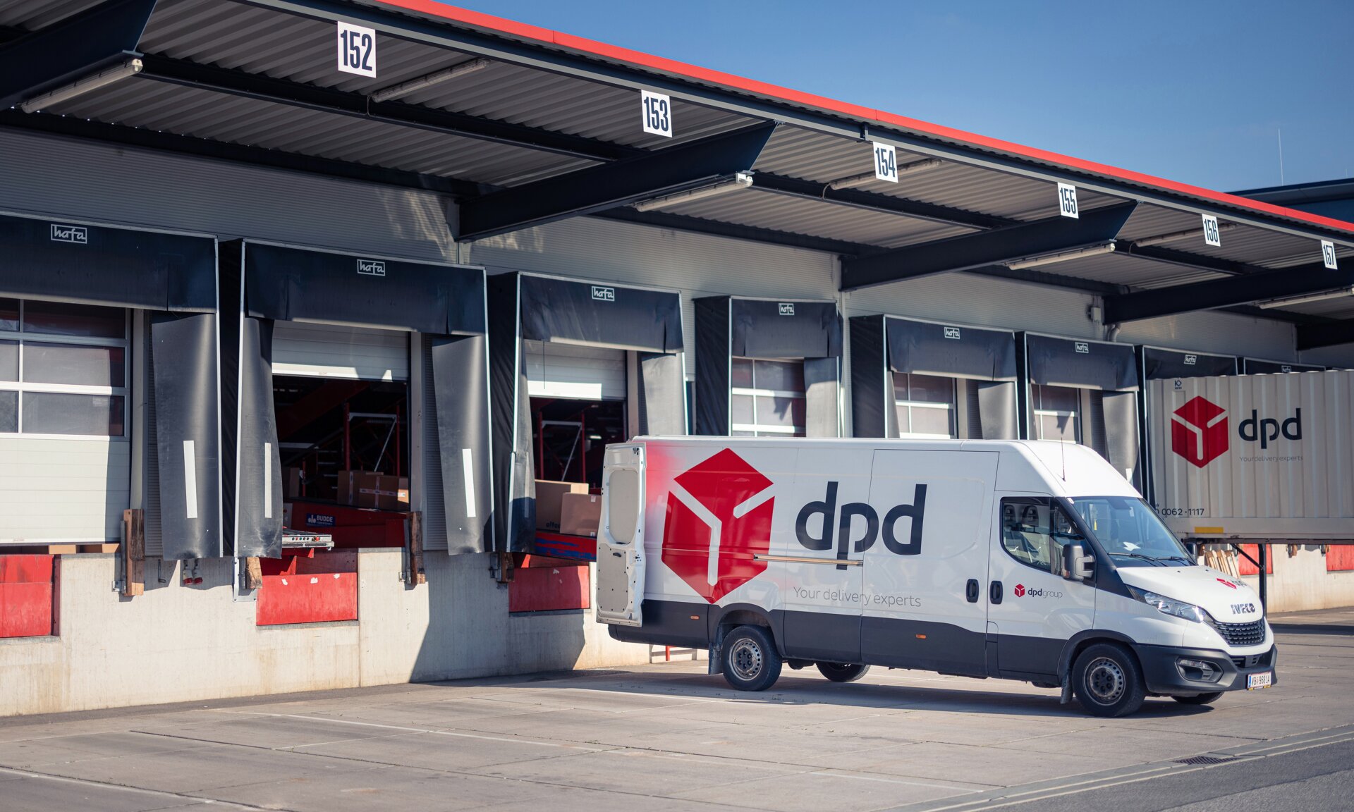 Es steht ein dpd Transporter vor einer Lagerhalle und wird mit Paketen beladen