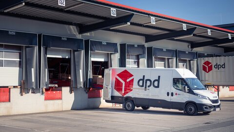 Es steht ein dpd Transporter vor einer Lagerhalle und wird mit Paketen beladen