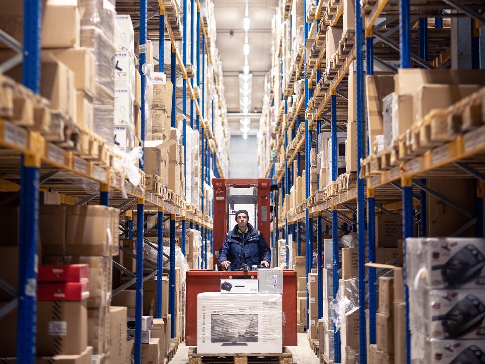 Es faehrt ein Gabelstapler in einer Paketversand Halle auf Fokus zu