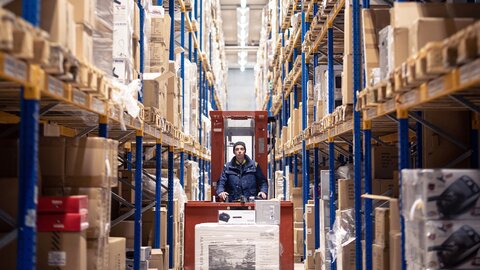 Es faehrt ein Gabelstapler in einer Paketversand Halle auf Fokus zu