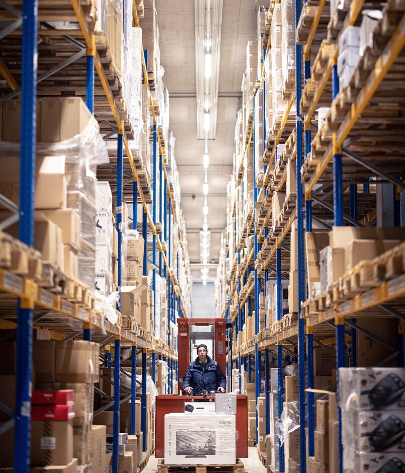 Es faehrt ein Gabelstapler in einer Paketversand Halle auf Fokus zu