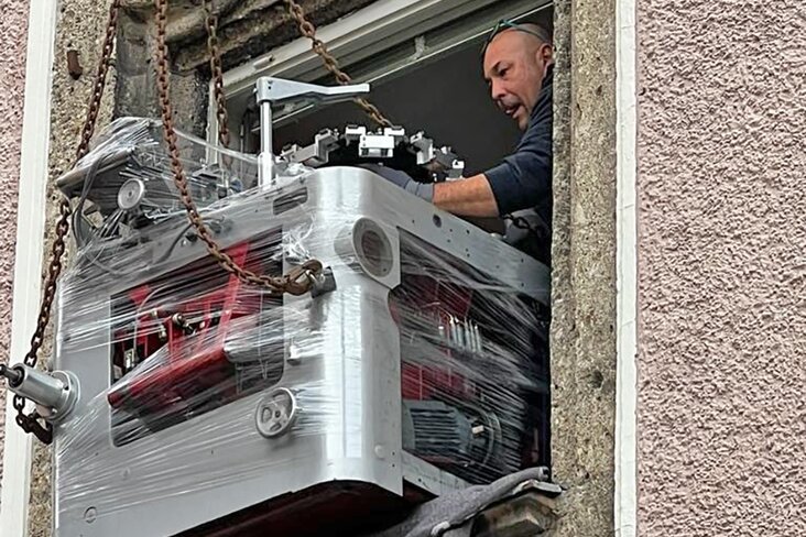 Maschine wird durch Fenster mit Kran transportiert.