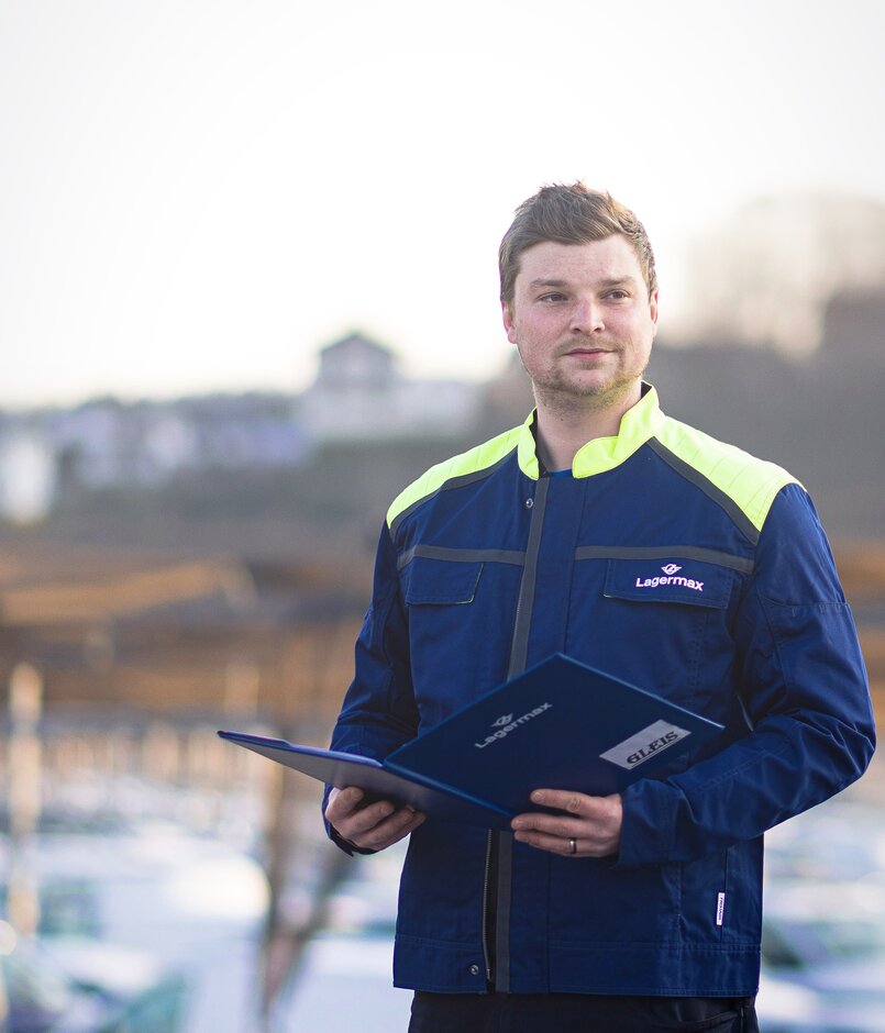 Lagermax Arbeiter hat Arbeitsmappe und Blick in die Ferne.