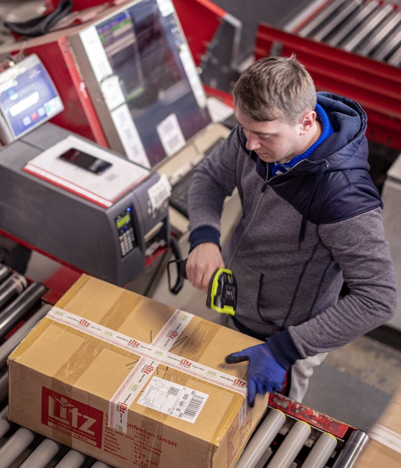 Ein Arbeiter steht vor Rollband und macht eine ID Pruefung beim Paketversand der dpd primetime