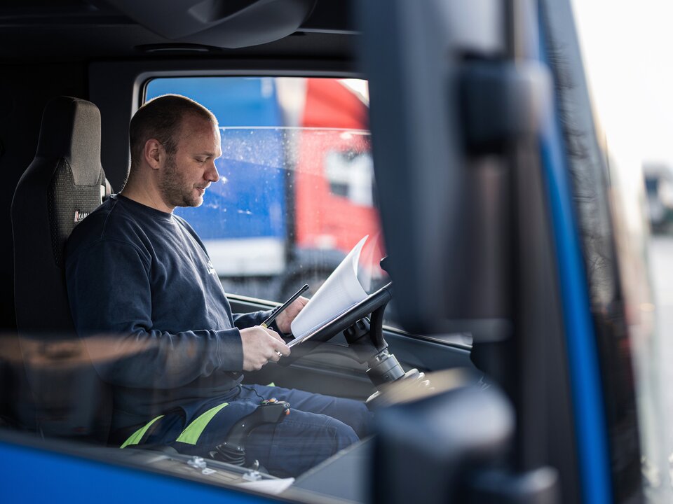 Ein Arbeiter sitzt in einer LKW Fahrerkabine und sieht sich Dokument an