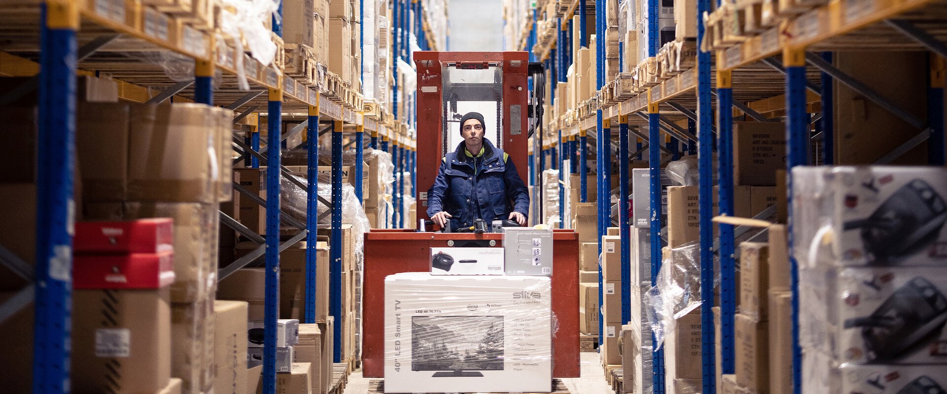 Es faehrt ein Gabelstapler in einer Paketversand Halle auf Fokus zu