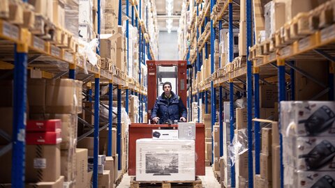 Es faehrt ein Gabelstapler in einer Paketversand Halle auf Fokus zu