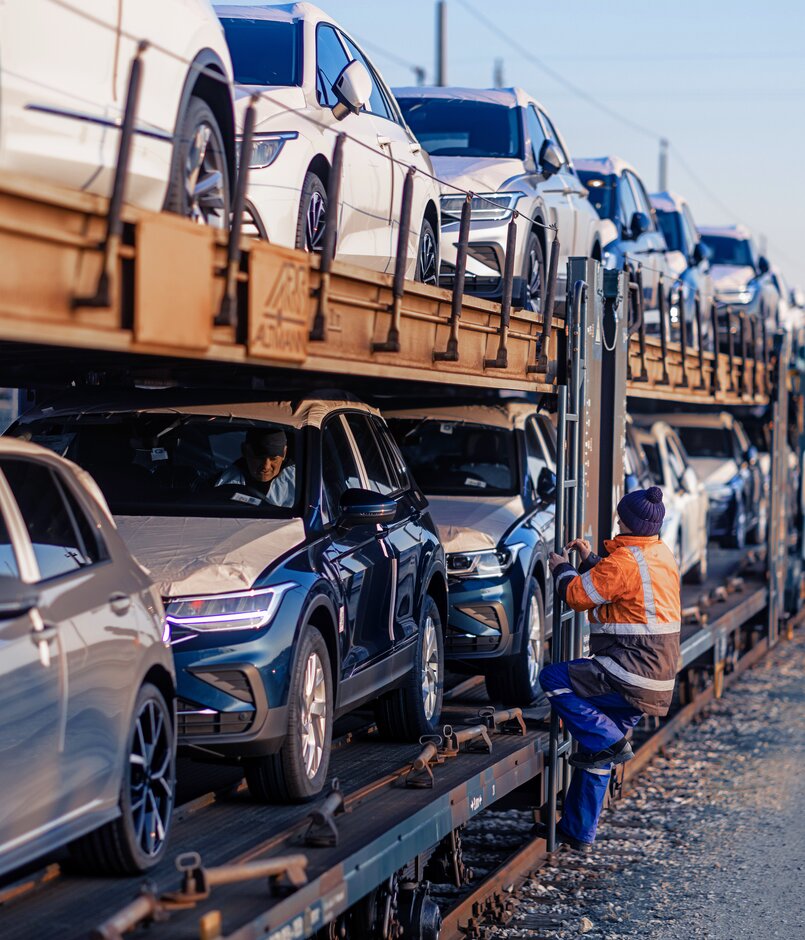 Lagermax Arbeiter klettert auf Auto Transport Gueterzug in der Seitenansicht.