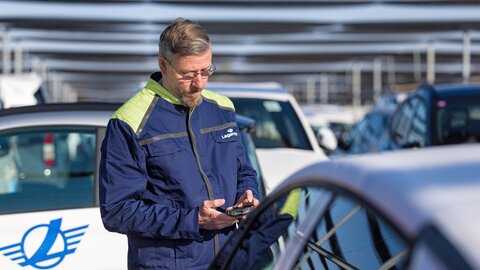 Ein Arbeiter blickt auf Mobilgeraet zwischen Autos in der Nahansicht