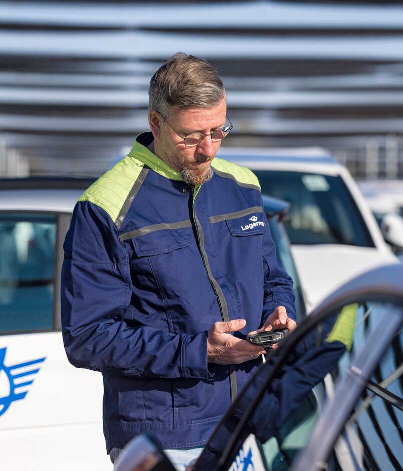 Ein Arbeiter blickt auf Mobilgeraet zwischen Autos in der Nahansicht