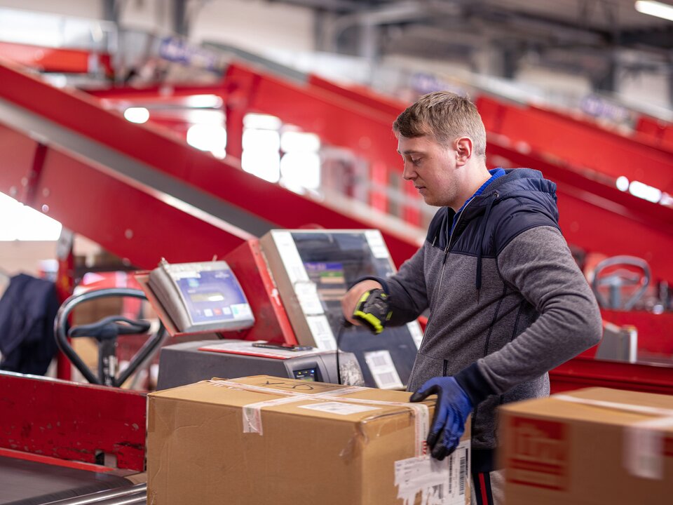 Ein Arbeiter scannt die ID eines Wertpakets auf einem Rollband im Rahmen vom Paketversand