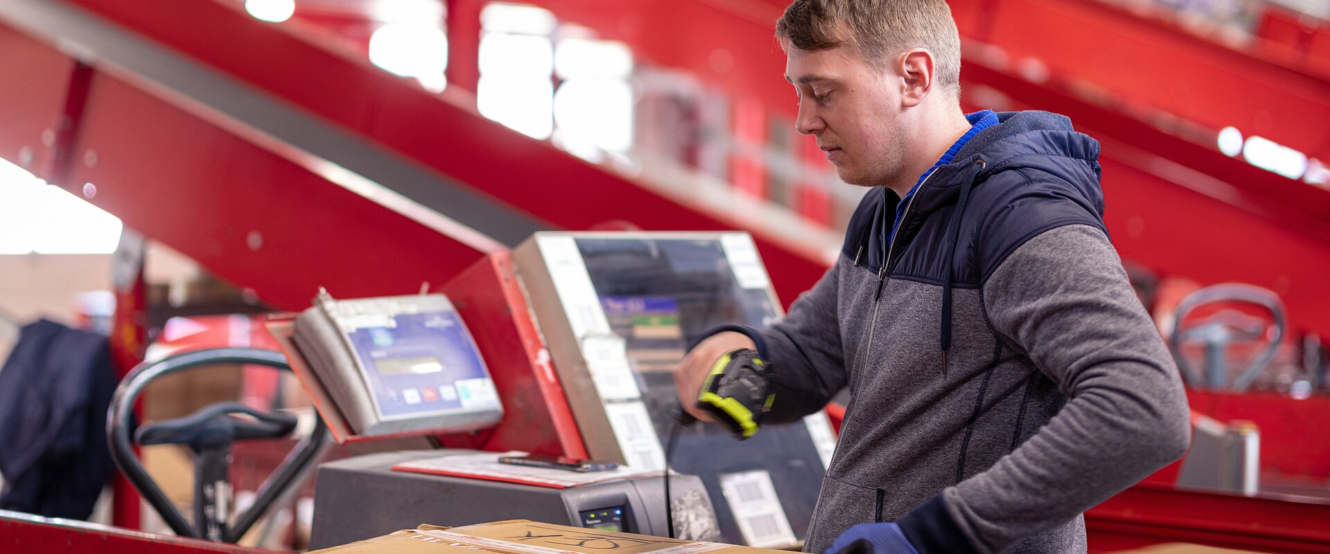 Ein Arbeiter scannt die ID eines Wertpakets auf einem Rollband im Rahmen vom Paketversand